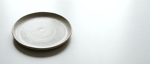Empty ceramic plate with natural glaze finish on white background, minimalist tableware for food presentation and culinary photography projects.