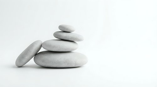 Stacked smooth gray stones balanced on white background, symbolizing zen, meditation, wellness, and spa relaxation therapy.