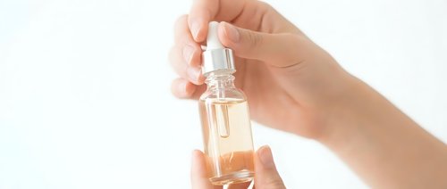 Female hand holding elegant glass perfume bottle with golden fragrance against clean white background for cosmetic and beauty product advertising.