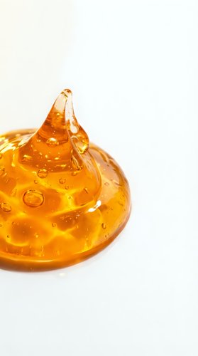 Golden amber gel or liquid forming a dome shape with a peak on white background, isolated for design use in cosmetics, skincare, wellness and beauty product packaging.