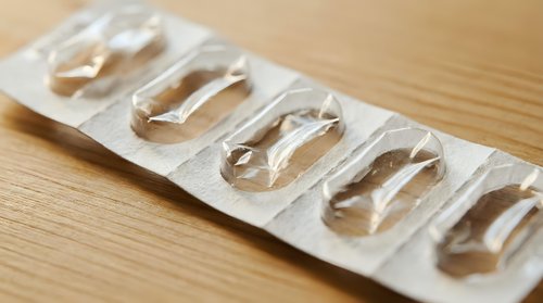 Clear gel capsules in blister pack on wooden surface for pharmaceutical and healthcare supplement packaging design applications.