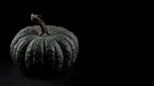 Textured dark gray pumpkin with stem isolated on black background, suitable for autumn designs, Halloween graphics, and seasonal marketing materials.