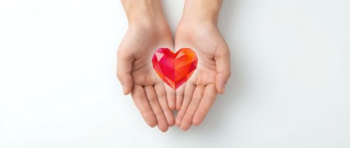 Hands gently holding red heart symbol on white background representing love, care, charity, healthcare, donation and compassion for wellness campaigns.