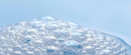 Clear soap bubbles floating on water surface with translucent foam texture creating abstract patterns for skincare and beauty product backgrounds.