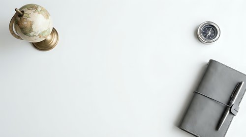 Flat lay of a globe, compass, and leather notebook with pen on a white background, evoking travel planning and adventure.