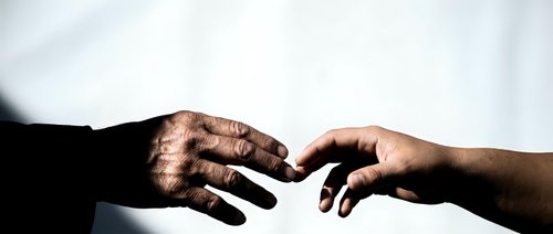 Two hands reaching toward each other in dramatic lighting, symbolizing connection, unity, and human touch against soft blurred background for emotional concepts.