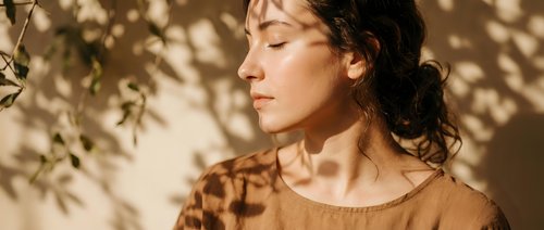 Young woman with curly hair enjoying warm sunlight and tree shadows on her face, peaceful moment of relaxation and mindfulness in natural outdoor setting.