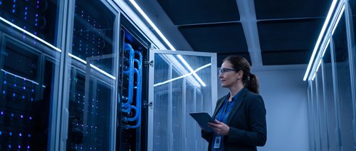Professional woman IT specialist working with tablet in modern server room with glowing blue LED lights and network equipment for technology solutions.