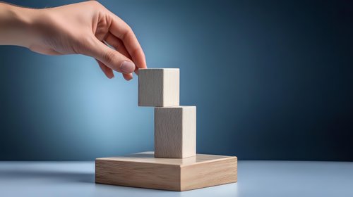 Female hand placing wooden cube block on stacked blocks against blue gradient background, representing business growth, strategy and development process.