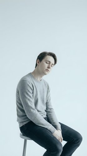Young man experiencing depression sitting on chair with closed eyes and tilted head showing mental health struggles and emotional exhaustion.