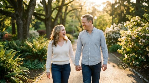 Mature couple holding hands while walking together on a tree-lined path during golden hour, enjoying outdoor leisure time and quality time together in nature.