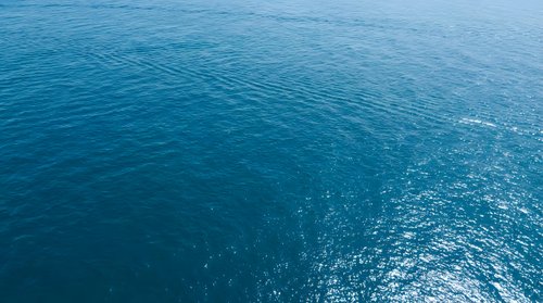 Deep blue ocean water surface with gentle ripples and sunlight reflections creating sparkling patterns across the vast seascape for marine backgrounds.