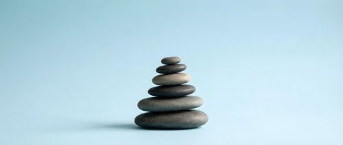 Balanced stack of smooth river stones creating zen meditation tower on clean white surface for wellness and mindfulness concepts.