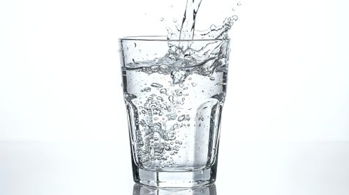 Clear glass filled with splashing water creating dynamic motion and bubbles against clean white background for refreshing beverage concepts.