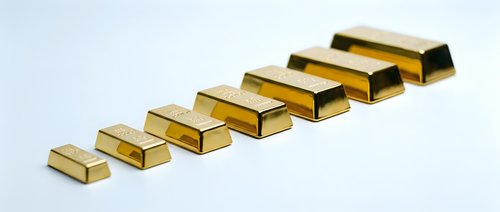 Golden metal bars arranged in ascending size order on white background representing wealth growth and financial investment success.