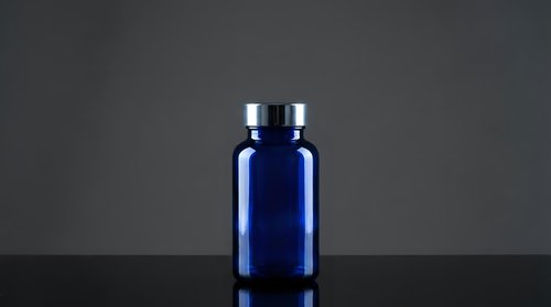 Blue glass pharmaceutical bottle with silver cap on dark background for medical packaging and supplement branding.