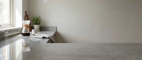 Modern minimalist kitchen interior with polished concrete countertops, white walls, natural light from window, and small potted herbs for contemporary home design.