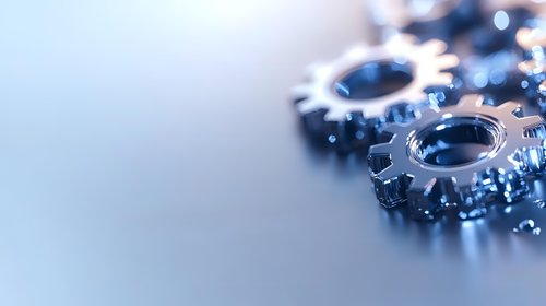Metallic gear wheels with blue tint on reflective surface, shallow depth of field creates soft background blur, highlighting industrial engineering concept.