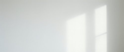 Minimalist interior with soft natural light casting geometric window shadows on neutral white wall, suitable for backgrounds and design projects.