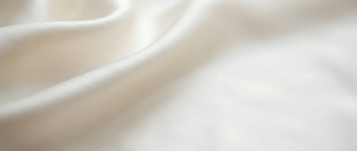 Soft cream colored fabric with gentle flowing waves and smooth texture creating elegant drapery folds for luxury textile and fashion design backgrounds.