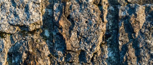 Rough textured rock surface with deep cracks and crevices showing natural weathering patterns and geological formations for backgrounds and textures.