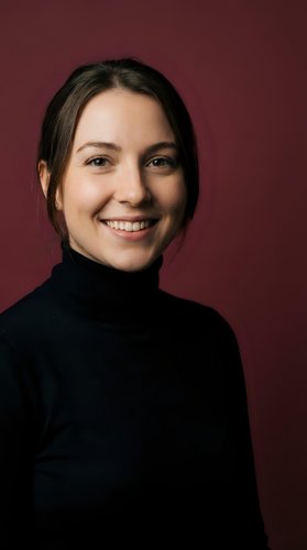 Young Caucasian woman in black turtleneck smiling warmly at camera against burgundy background for professional headshot and business portrait use.