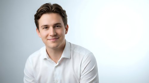 Young professional Caucasian businessman in white shirt smiling confidently at camera against clean studio background for corporate headshot photography.