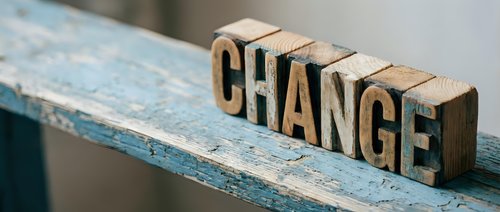 Wooden letterpress blocks spelling CHANGE on a rustic blue painted shelf, symbolizing transformation, growth, and new beginnings in business and life.