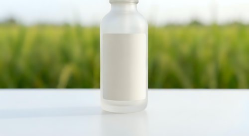White glass milk bottle with blank label on wooden table against blurred green farm field background for dairy product packaging and agricultural marketing.