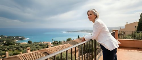 Professional female chef in white uniform standing on Mediterranean terrace overlooking azure sea and coastal landscape for culinary tourism concepts.