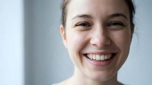 Young Caucasian woman with natural makeup smiling broadly showing white teeth in bright modern interior setting for lifestyle and wellness content.