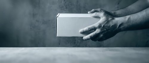 Male hands holding white blank box package against concrete wall background for product presentation and mockup design purposes.