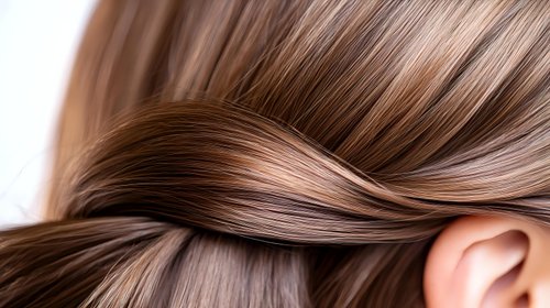 Silky smooth brown hair close-up showing healthy, shiny strands twisted in an elegant wave pattern against soft natural lighting, demonstrating hair care and beauty concepts.