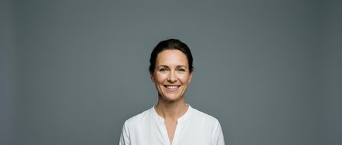Professional smiling businesswoman in white shirt against gray background for corporate presentations and marketing materials.