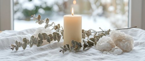 Peaceful spa arrangement with burning candle, eucalyptus branches and white towels on marble surface creating relaxing wellness atmosphere for meditation.