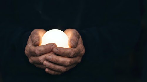 Hands holding glowing sphere against dark background, symbolizing hope, energy, innovation, and spiritual power for business and wellness concepts.