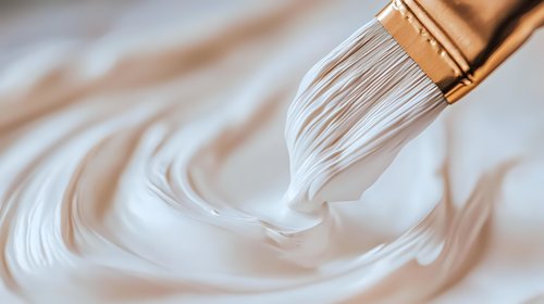 Artistic close-up of white paint swirling from paintbrush bristles creating smooth circular patterns against neutral background, showing fluid creative motion.