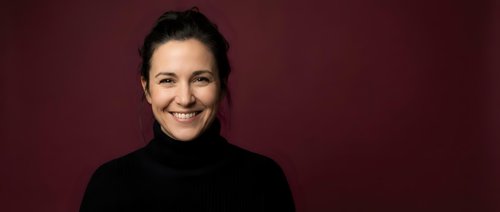 Smiling middle-aged Caucasian woman in black turtleneck sweater against burgundy background for professional headshot and business portrait photography.