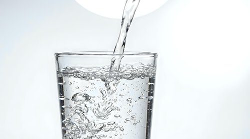Clear water pouring into transparent glass with bubbles and splash creating refreshing drink concept for health and hydration lifestyle.