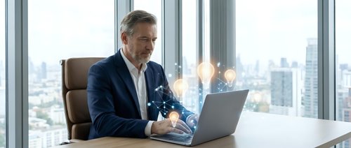 Middle-aged Caucasian businessman in suit working on laptop with glowing digital light bulb hologram, innovation and technology concept in modern office.