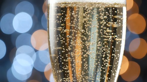 Champagne glass with golden bubbles against festive bokeh lights background for New Year celebration and holiday toasting moments.
