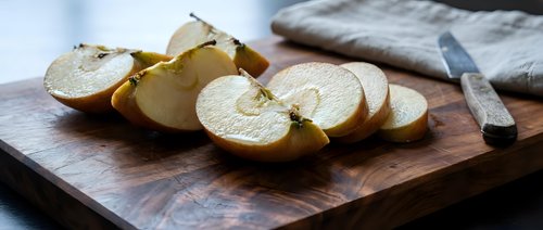 Fresh sliced apples on wooden cutting board with knife, healthy snacking and cooking preparation concept for kitchen and food photography.