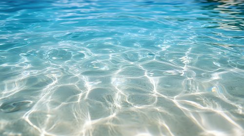 Tranquil turquoise water surface with sunlight creating rippling patterns and reflections, crystal clear shallow sea showing sandy bottom through transparent waves.