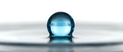 Transparent blue glass sphere resting on reflective wet surface with ripples, isolated on white background for design and commercial use.