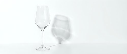 Two elegant wine glasses on white background, one standing upright and one lying down, creating artistic shadows for minimalist design concepts.
