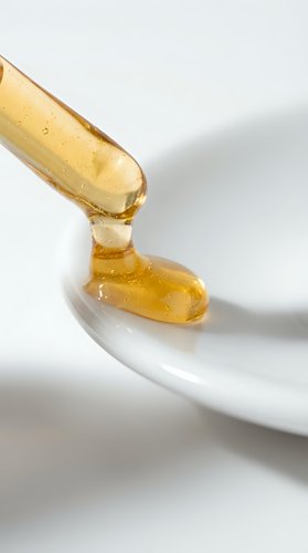 Golden honey dripping from wooden dipper onto white ceramic bowl, showcasing natural sweetener for culinary, wellness, and food styling applications.