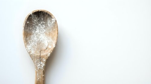 Wooden spoon with flour powder on white background for baking and cooking projects.