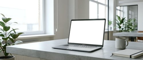 Modern laptop with blank white screen on minimalist desk workspace with plants and coffee mug in bright office interior for mockup presentations.