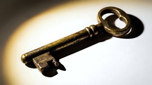 Antique brass skeleton key with dramatic shadow on light background, symbolizing mystery, security, and access.