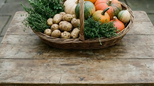 Wicker basket filled with fresh organic vegetables including potatoes, pumpkins, and herbs on rustic wooden surface for autumn harvest and farm market designs.
